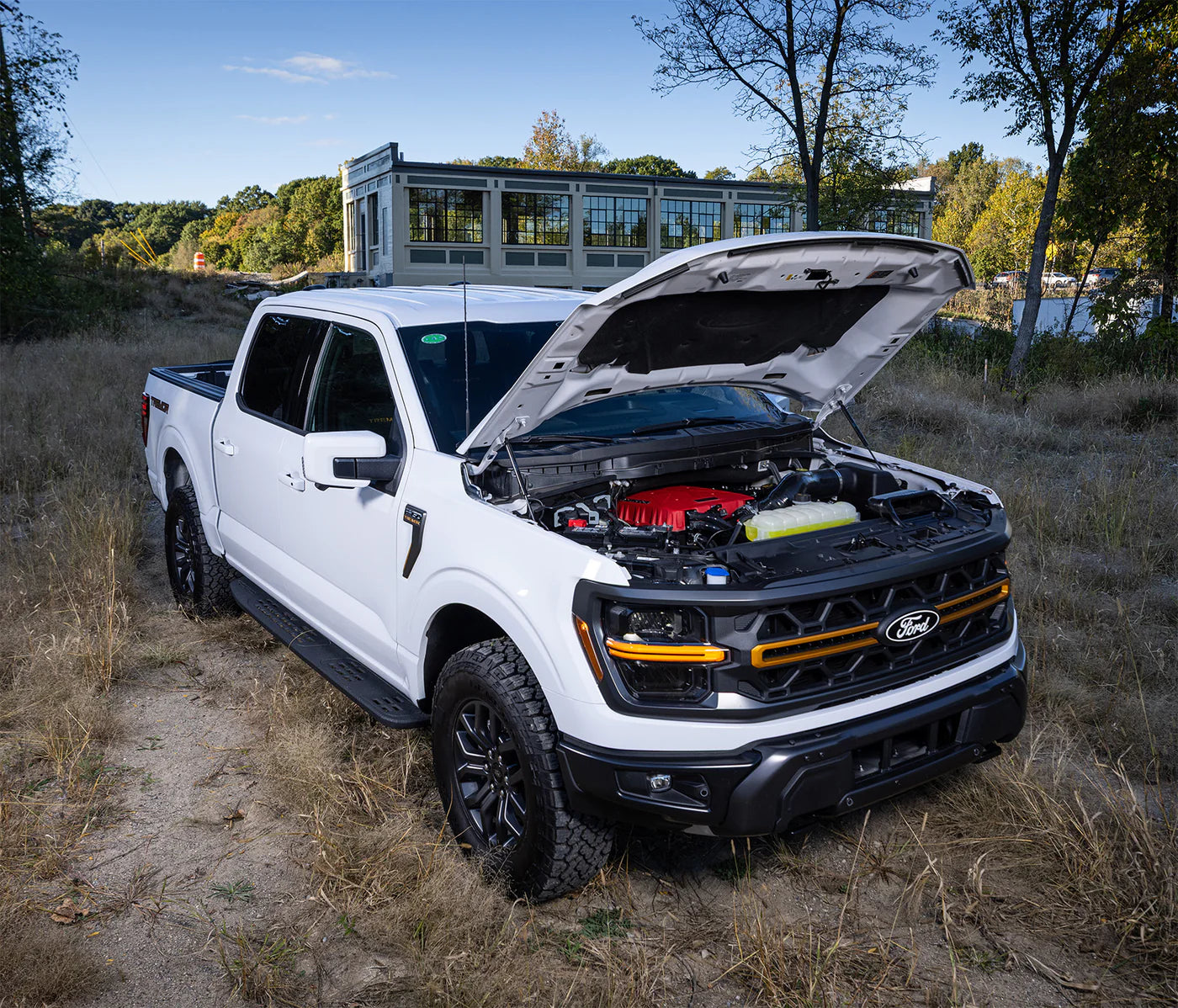 White Ford F-150 truck parked on grass with hood open, showing engine with red supercharger component.